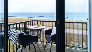Un balcón con vistas al mar, que incluye una mesa con un frutero y una silla.