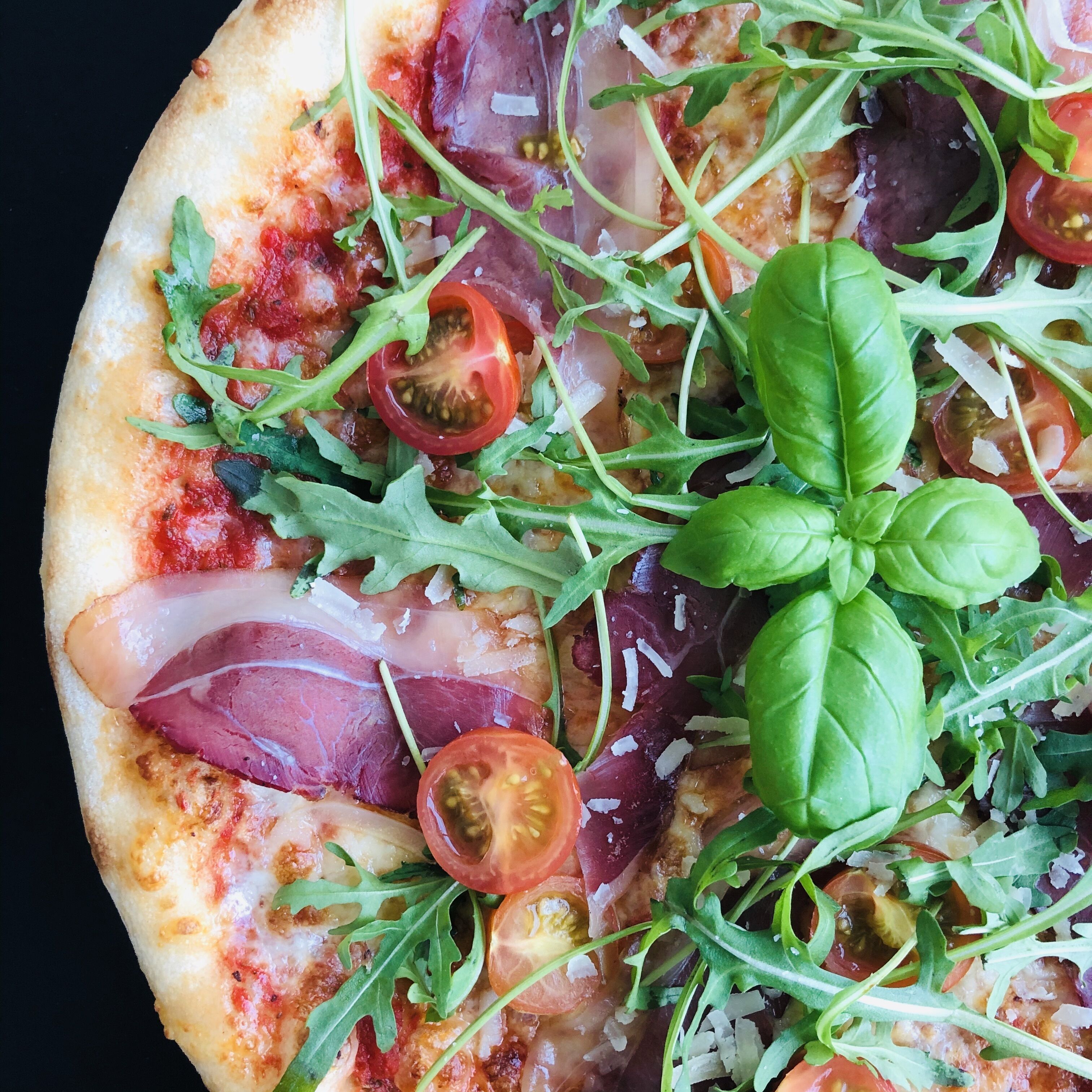 A pizza with various toppings including arugula, tomatoes, and cheese.