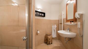 Un baño con mampara de vidrio, lavamanos, espejo y toallero.