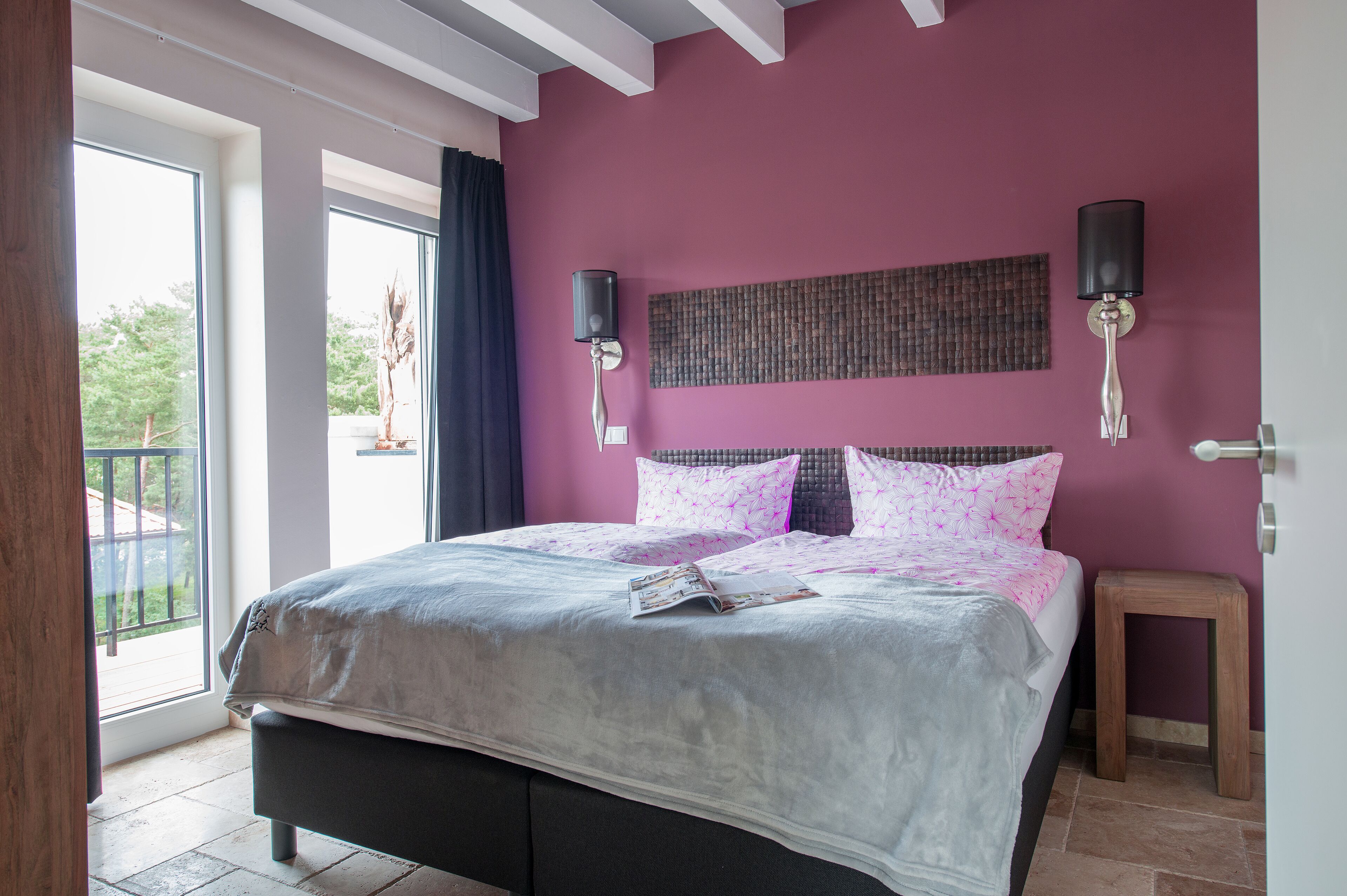Quarto com cama grande, duas luminárias fixadas na parede e vista para o verde lá fora.