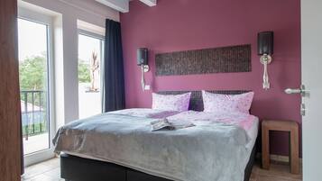 A bedroom with a large bed, two wall-mounted lamps, and a view of greenery outside.