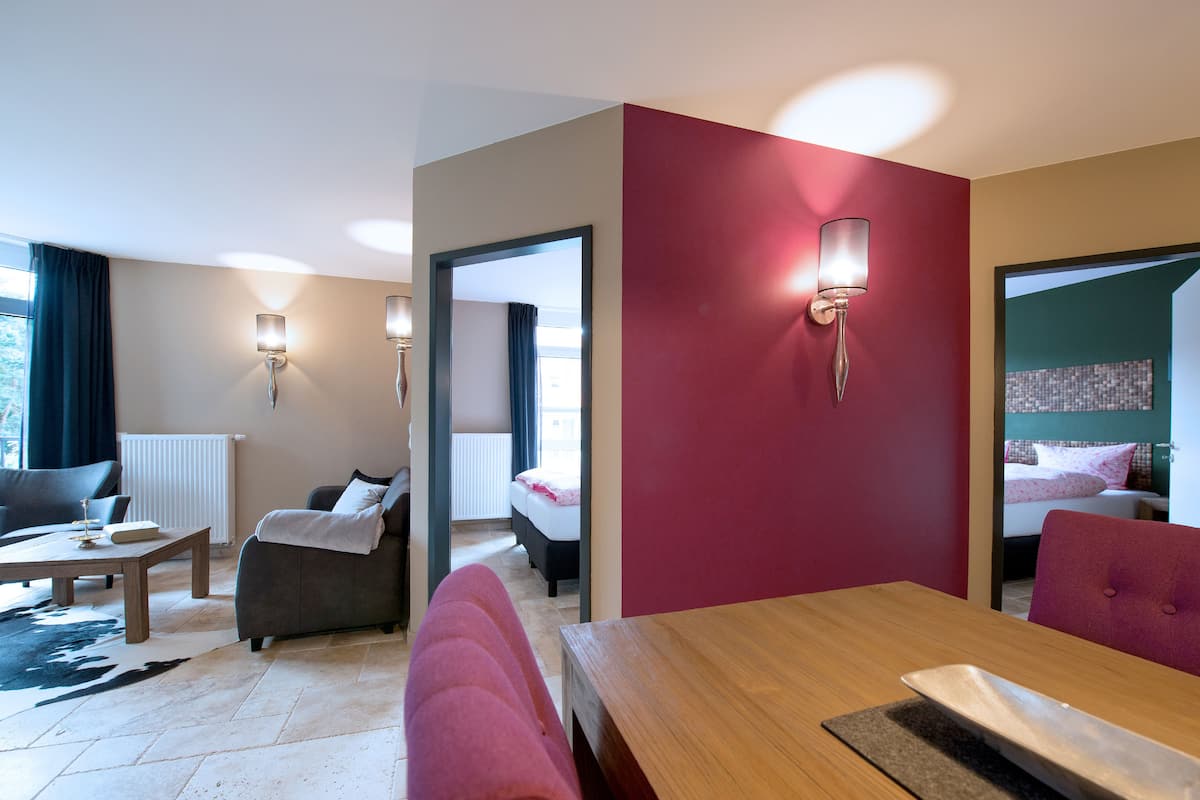 Une chambre d’hôtel avec un canapé, une table en bois, un lit et un mur d’accent de couleur rouge.