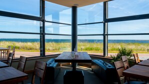 Un restaurante con amplios ventanales que ofrece vistas al océano y campos verdes.
