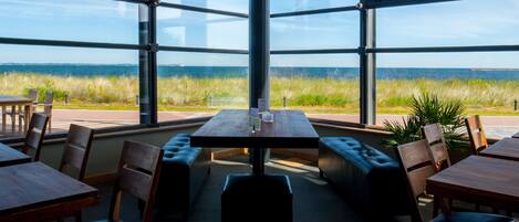 A restaurant with large windows offering a view of the ocean and grassy fields.