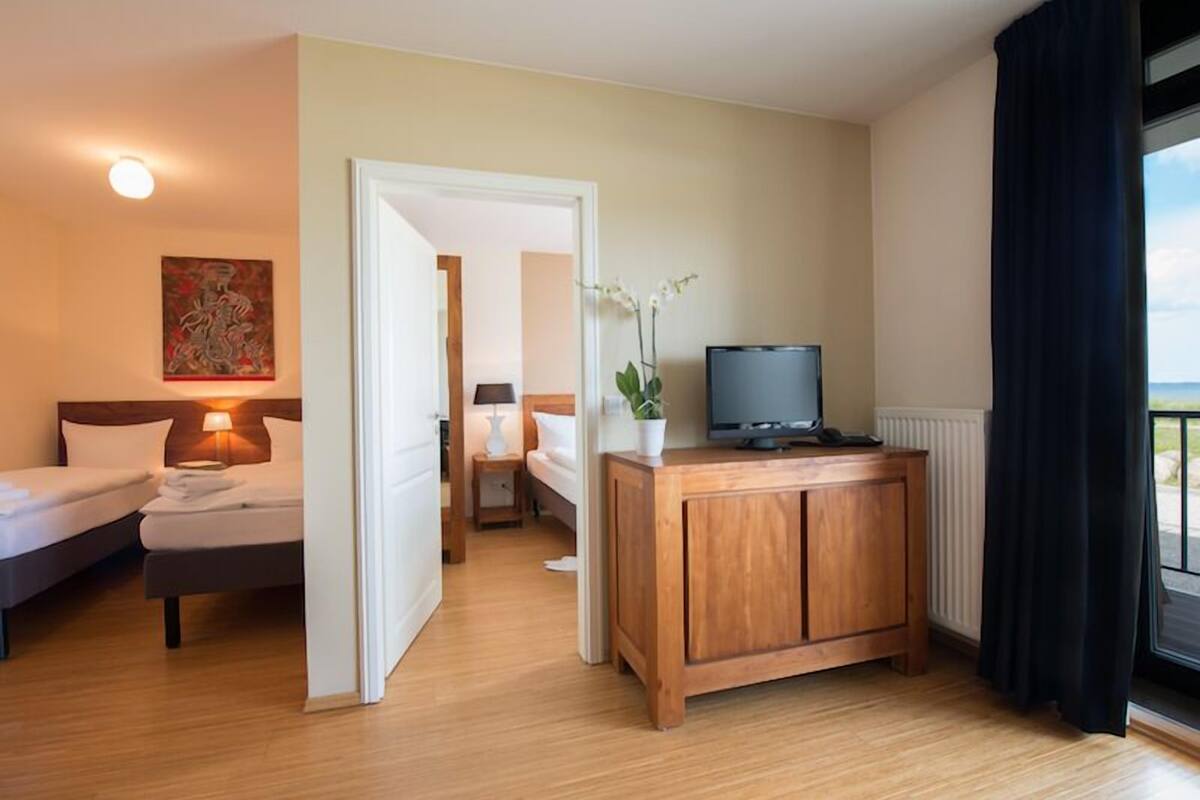 Une chambre d’hôtel avec deux lits, une armoire en bois avec un téléviseur, une orchidée en pot et une vue sur la mer par la fenêtre.