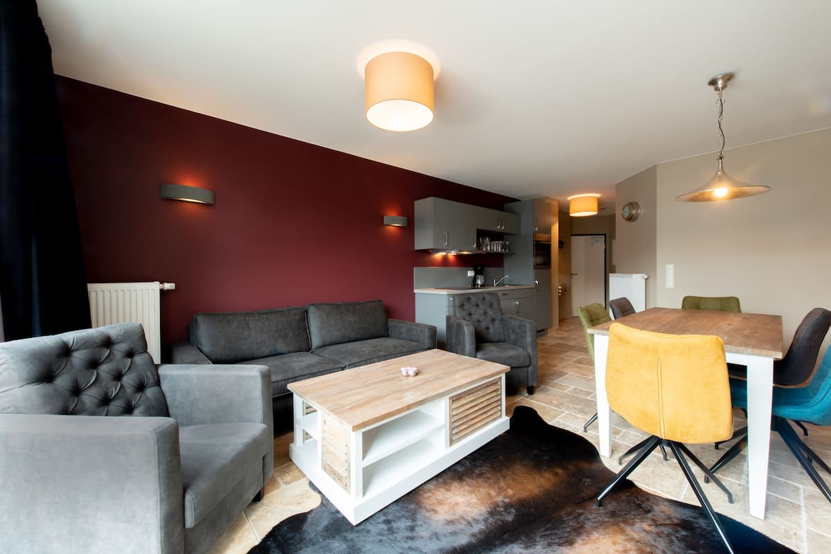 Un salon moderne avec un canapé gris, une table basse en bois et un coin repas comprenant une table en bois et des chaises jaunes.