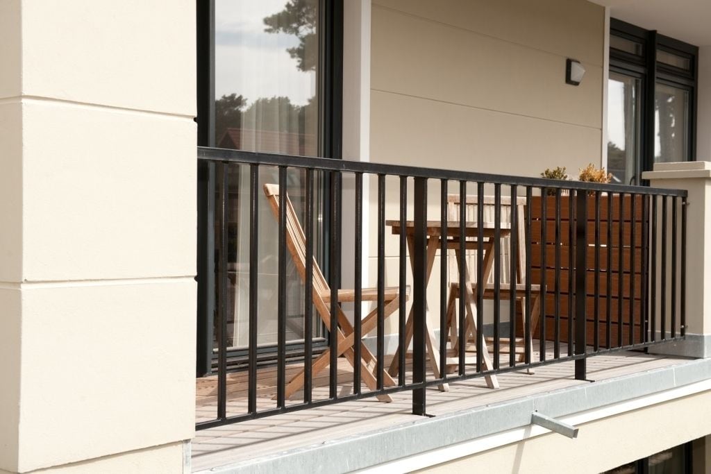 A balcony with a black railing, a wooden table, and chairs.