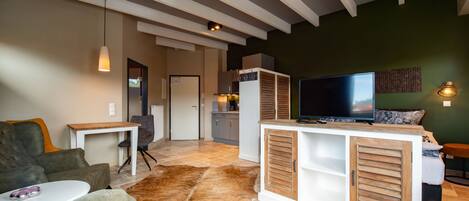A modern living room with a large TV, a dining area, and a kitchen in the background.