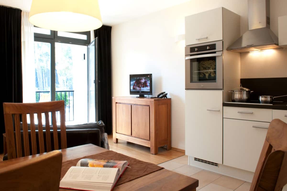 Une cuisine moderne avec un coin repas, un téléviseur posé sur un meuble et une fenêtre avec des rideaux.