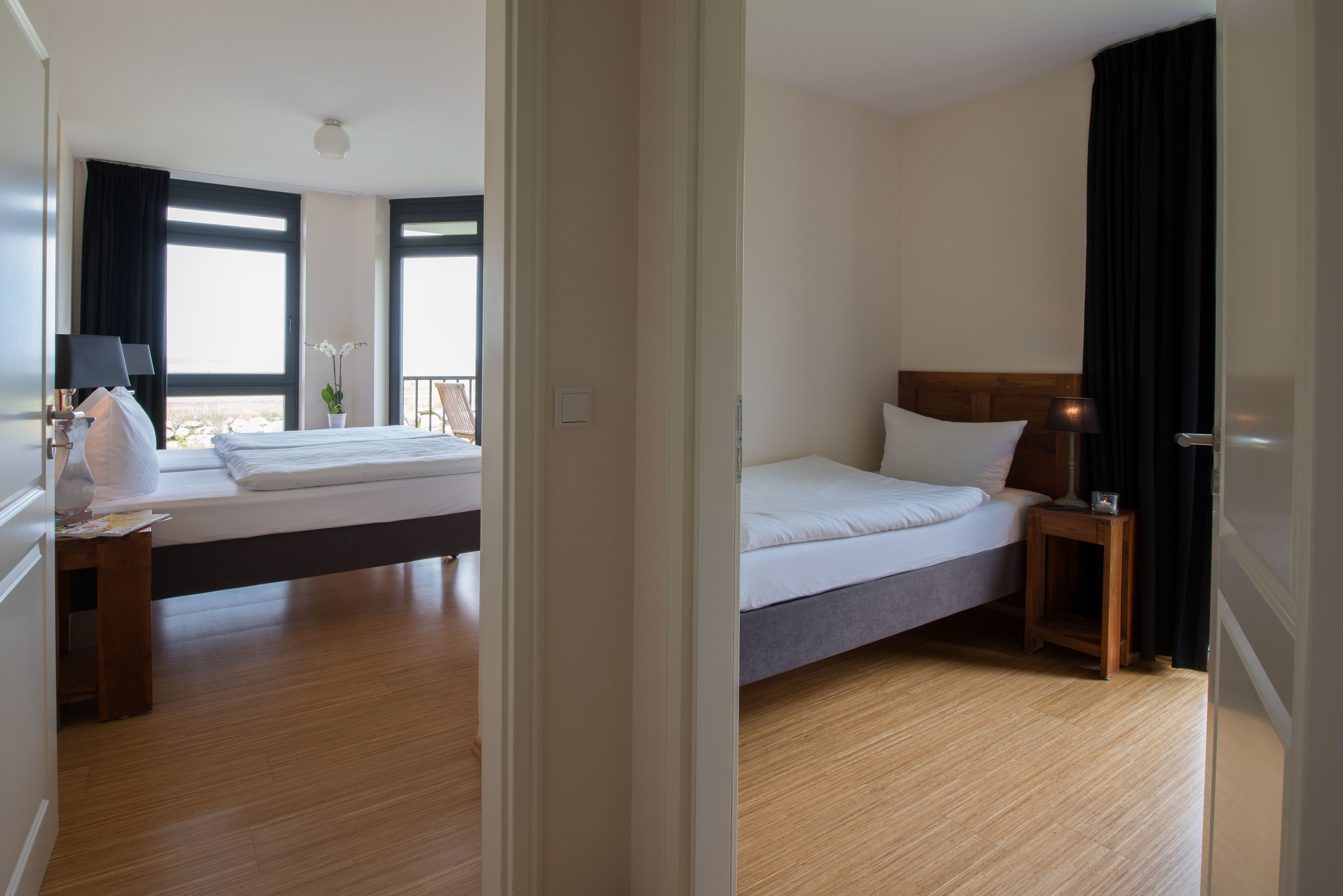 Habitación de hotel con una cama grande, una mesita de noche con lámpara, una pequeña mesa con una planta y vistas al exterior a través de una ventana.