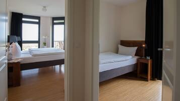 Habitación de hotel con una cama grande, una mesita de noche con lámpara, una pequeña mesa con una planta y vistas al exterior a través de una ventana.