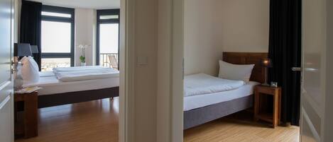 Habitación de hotel con una cama grande, una mesita de noche con lámpara, una pequeña mesa con una planta y vistas al exterior a través de una ventana.