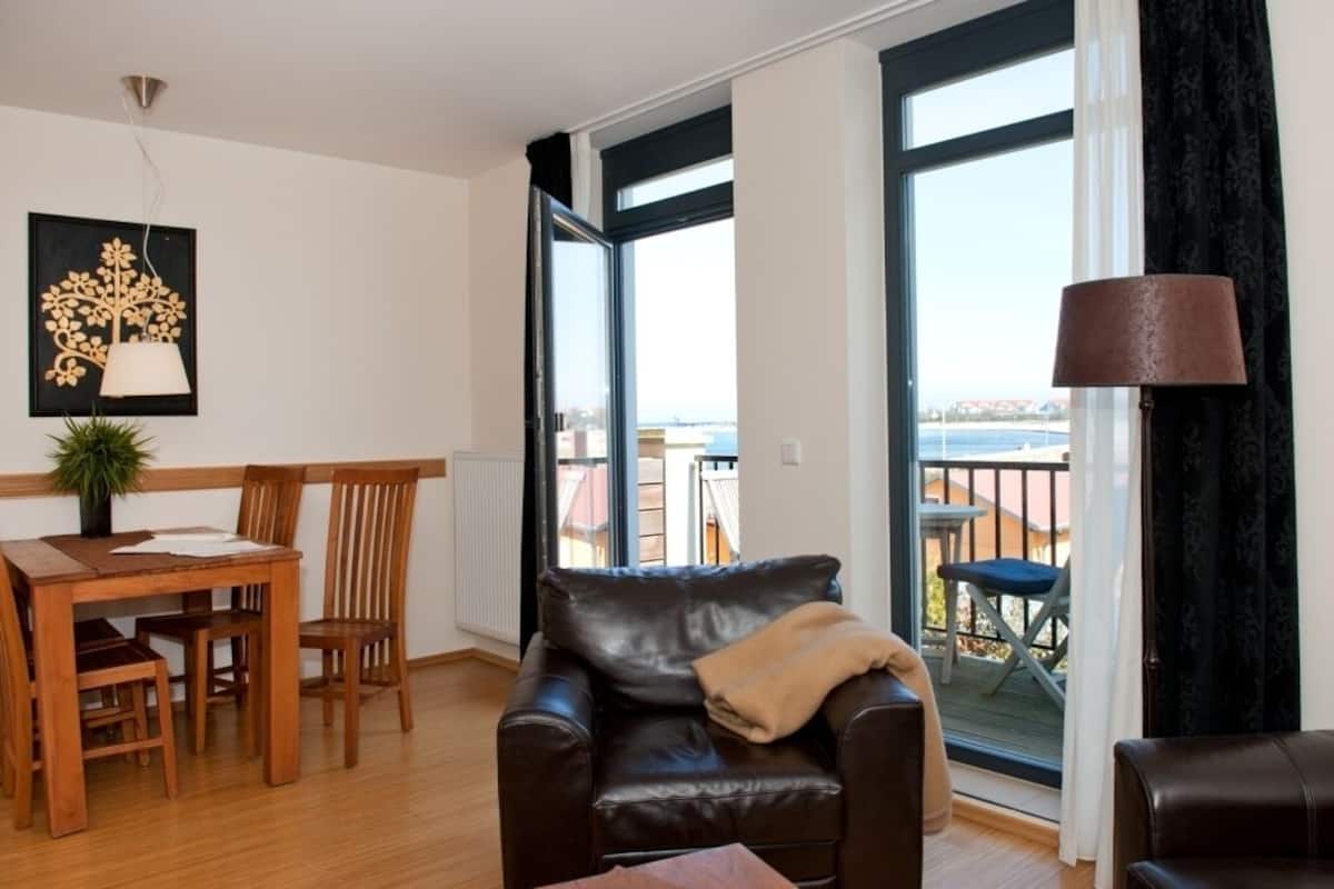Un salon avec un canapé en cuir, une table à manger avec des chaises, une plante en pot et une vue sur le balcon extérieur.