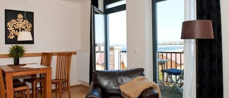 Un salon avec un canapé en cuir, une table à manger avec des chaises, une plante en pot et une vue sur le balcon extérieur.