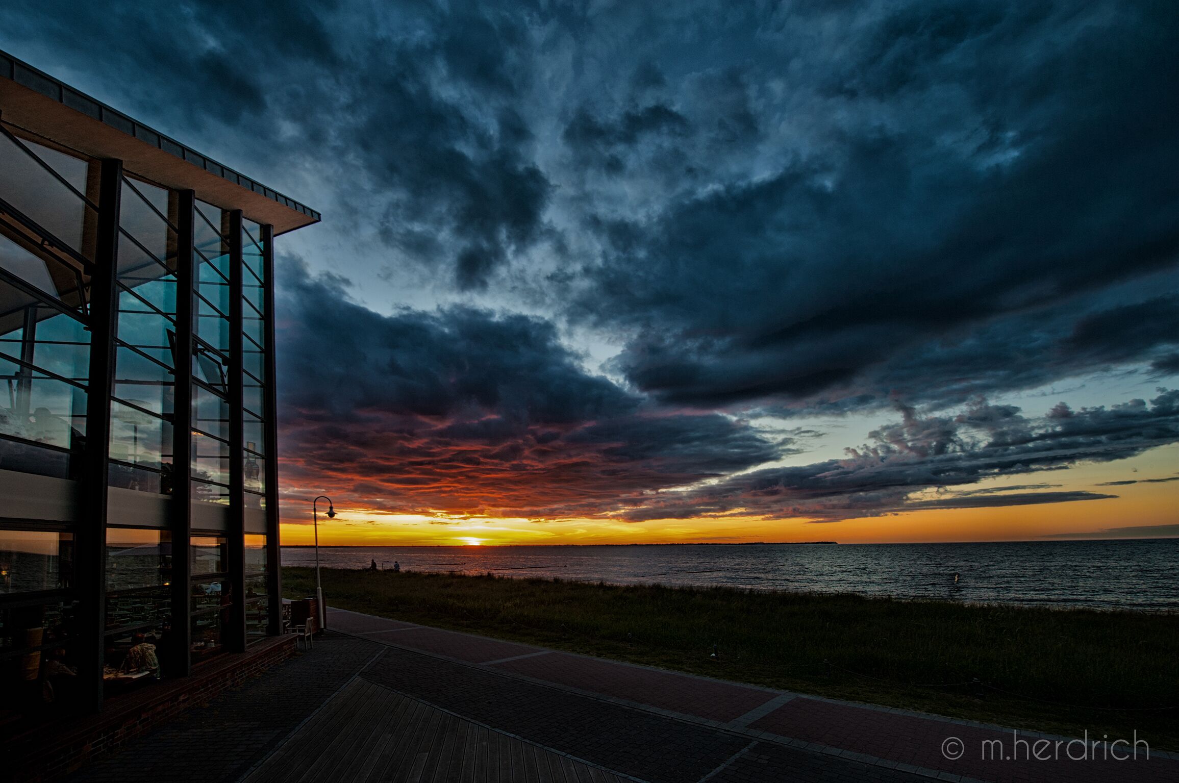 Un bâtiment moderne doté de grandes fenêtres en verre donnant sur une plage au coucher du soleil.