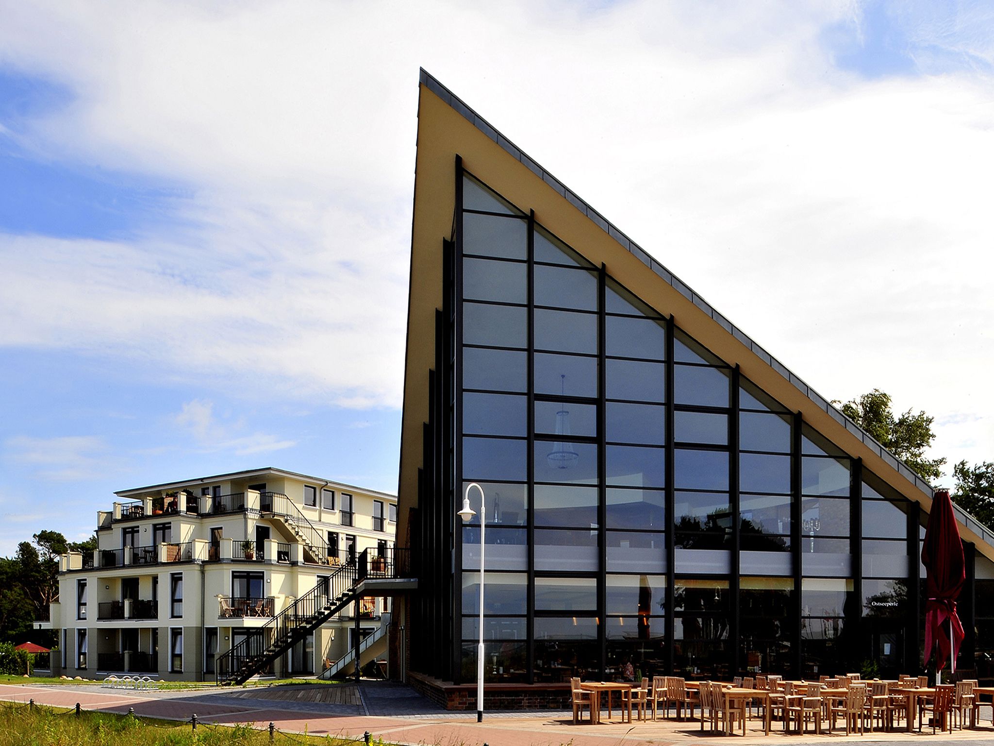 A modern building with a large glass facade, outdoor seating area, and a staircase leading to an upper level.