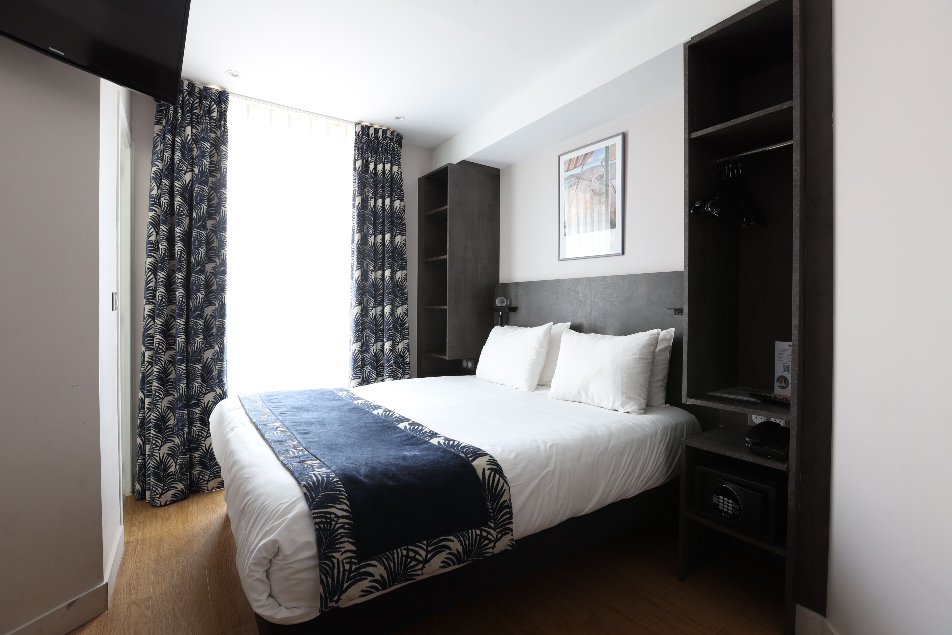 Quarto de hotel com cama, guarda-roupa, escrivaninha e janela com cortinas.