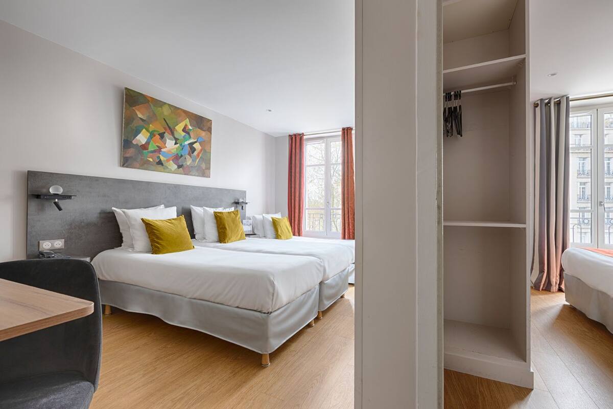 A modern hotel room with two beds, a desk, and a wardrobe.