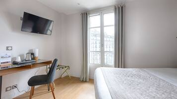 A hotel room with a bed, a desk with a chair, a television, and a window with curtains.