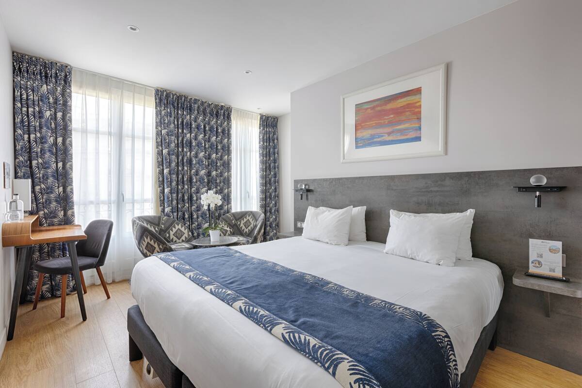 A hotel room with a large bed, a desk, a chair, and a small table with a potted plant.