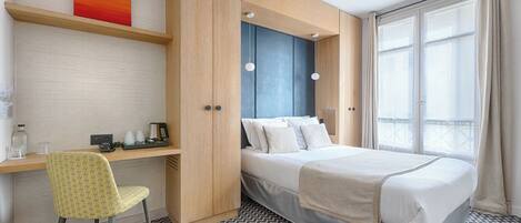 Una habitación de hotel con cama, escritorio, silla y un ventanal grande.