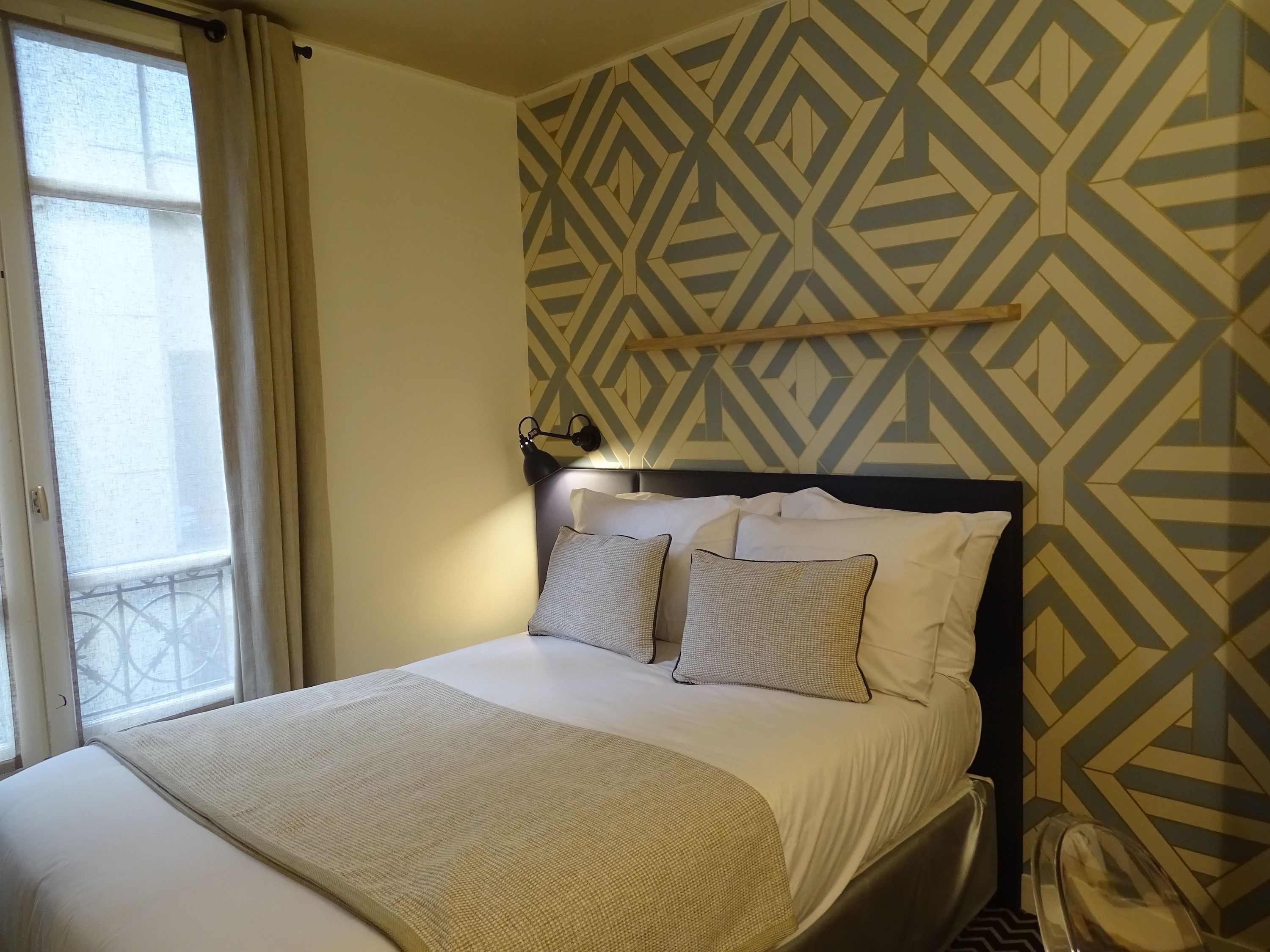 Un lit bien fait, avec une tête de lit, une lampe de chevet et un papier peint à motifs.