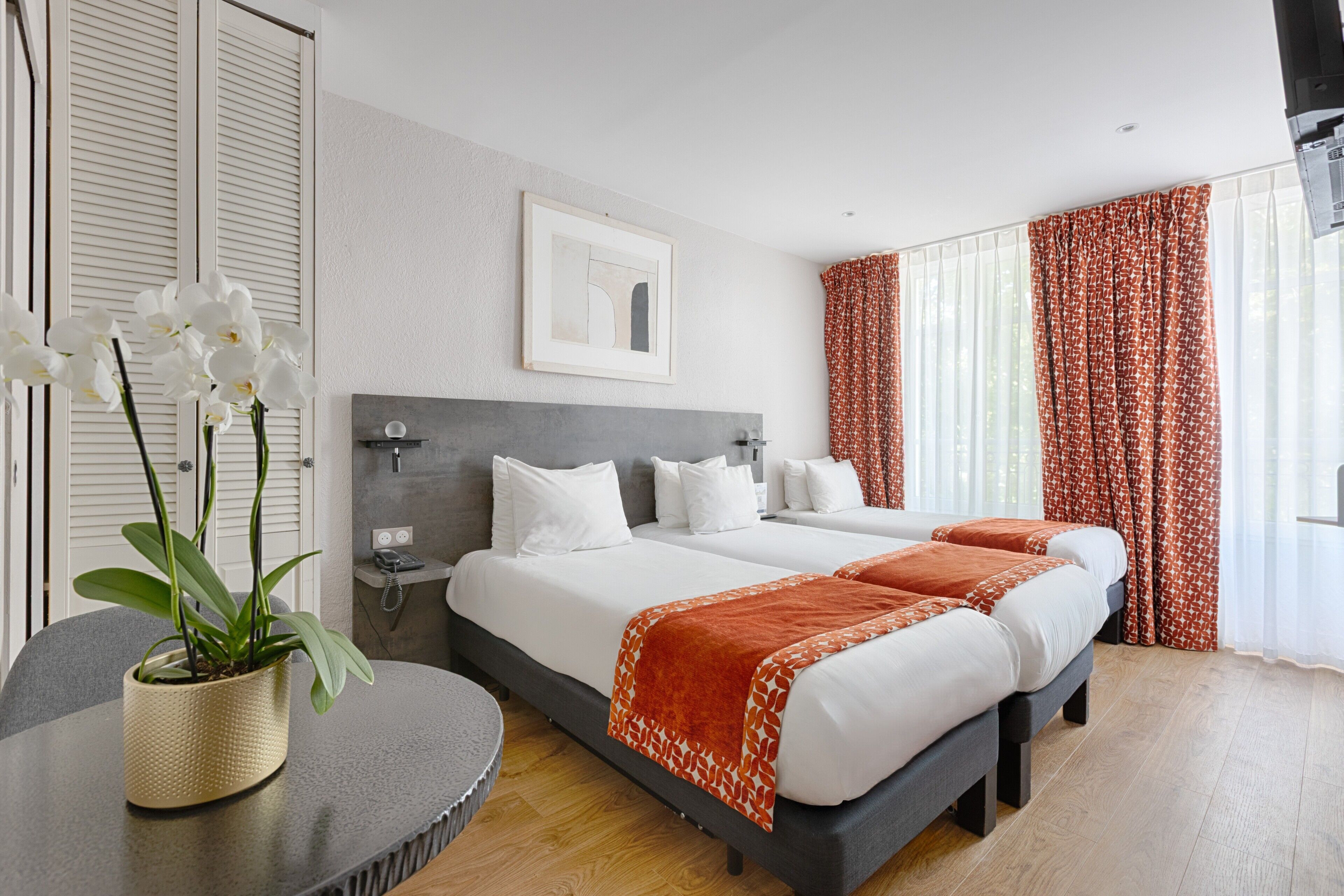 Une chambre d’hôtel avec deux lits, une table de chevet, une plante en pot et un tableau encadré au mur.