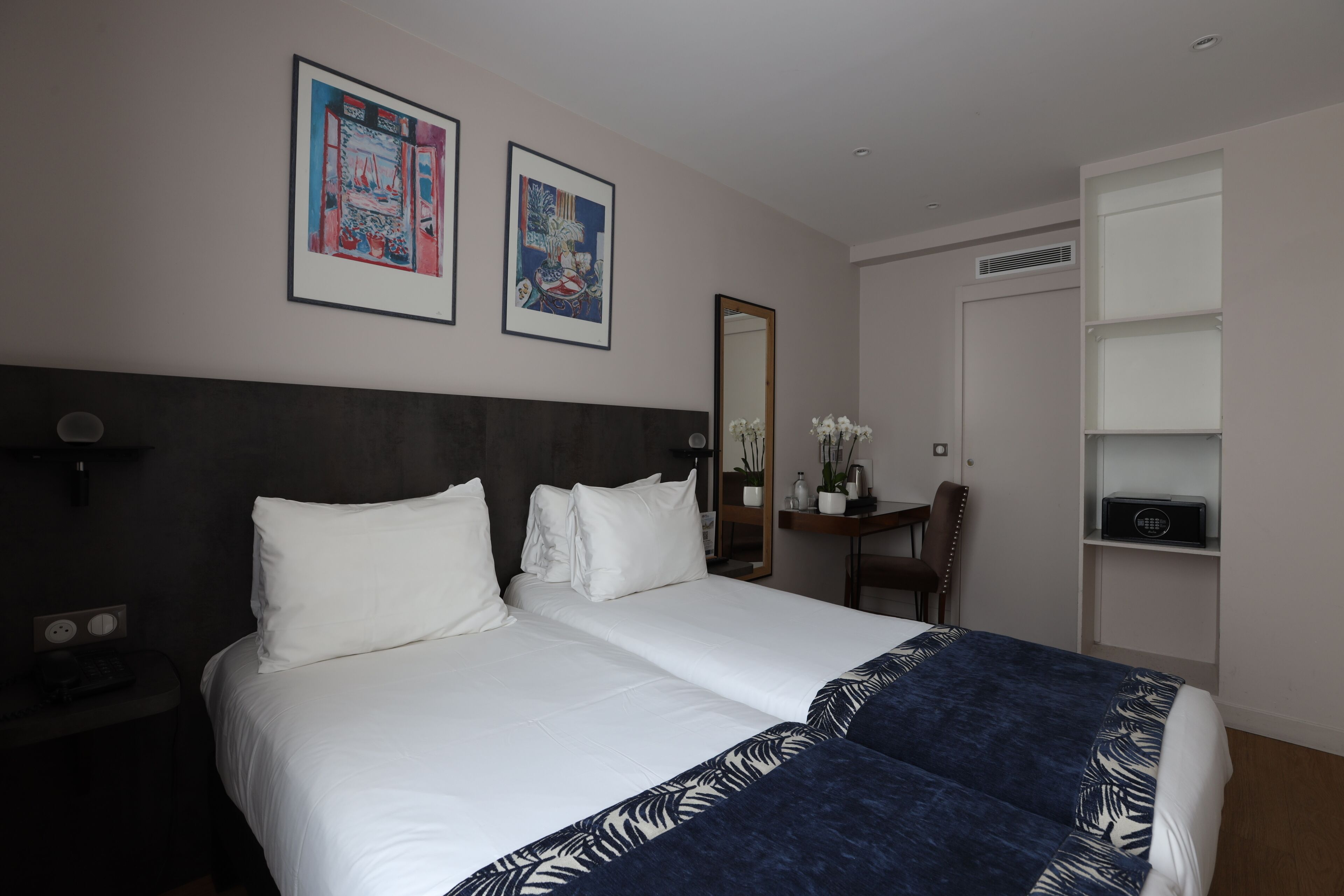 A hotel room with two beds, a desk with a chair, a mirror, and a shelf with a radio.
