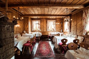 A rustic wooden dining room with multiple tables and chairs, a patterned rug, and a wooden cabinet.