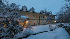 Ein großes, mehrstöckiges Gebäude mit verschneiter Umgebung, das eine markante Eingangshalle und beleuchtete Fenster hat.