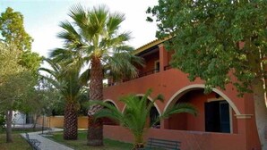 A building with a red facade, arched windows, and a pathway leading to a bench. - Sungate (Corfu)
