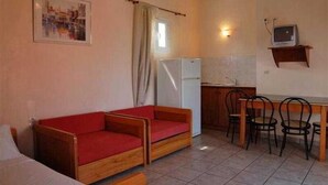 A compact room with a wooden sofa, a small dining table with chairs, a refrigerator, and a television on a shelf. - Sungate (Corfu)