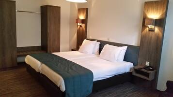 A hotel room with a large bed, a nightstand, a wardrobe, and two wall-mounted lights.