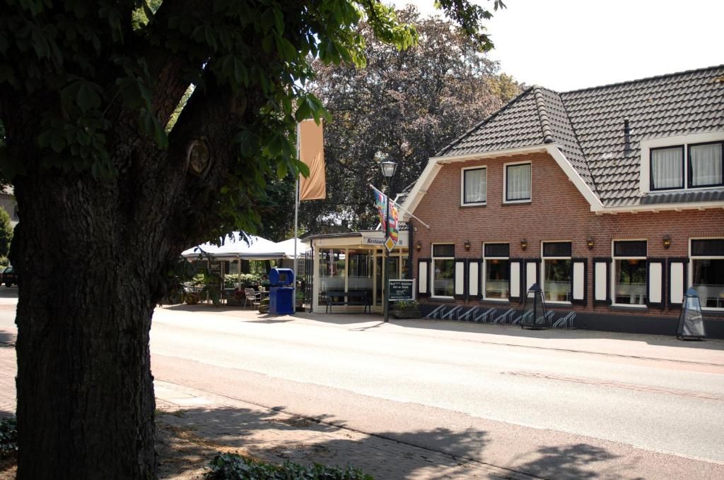A street view with a building featuring a brick facade, a covered outdoor seating area, and a tree in the foreground.