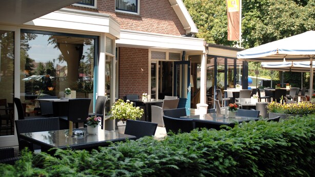 Ein Straßencafé mit Tischen, Stühlen und Grünpflanzen vor einem Backsteinhaus.