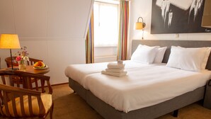 Ein Hotelzimmer mit einem großen Bett, einem Schreibtisch mit Lampe, einem Sessel und einem Fenster mit Vorhängen.