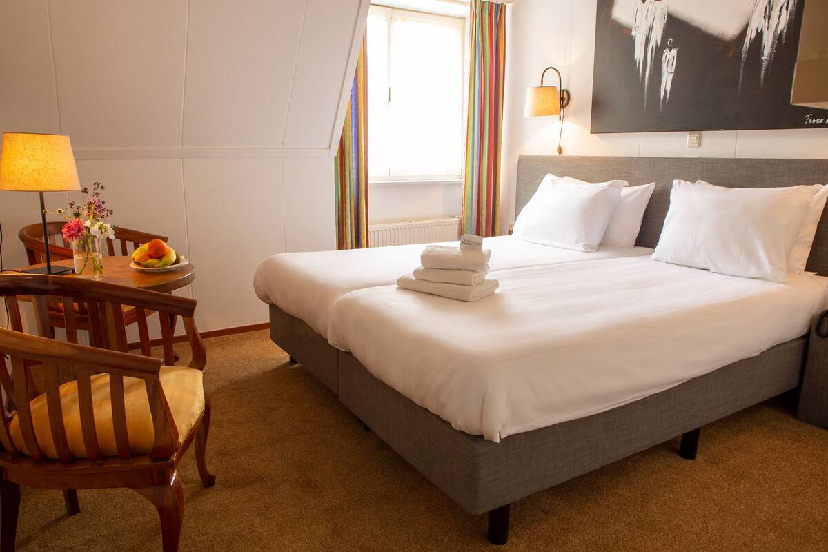 Ein Hotelzimmer mit einem großen Bett, einem Schreibtisch mit Lampe, einem Sessel und einem Fenster mit Vorhängen.