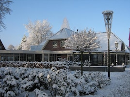 Um edifício com telhado coberto de neve, fachada de vidro e uma placa com os dizeres 'Hotel Restaurant Pizza'.