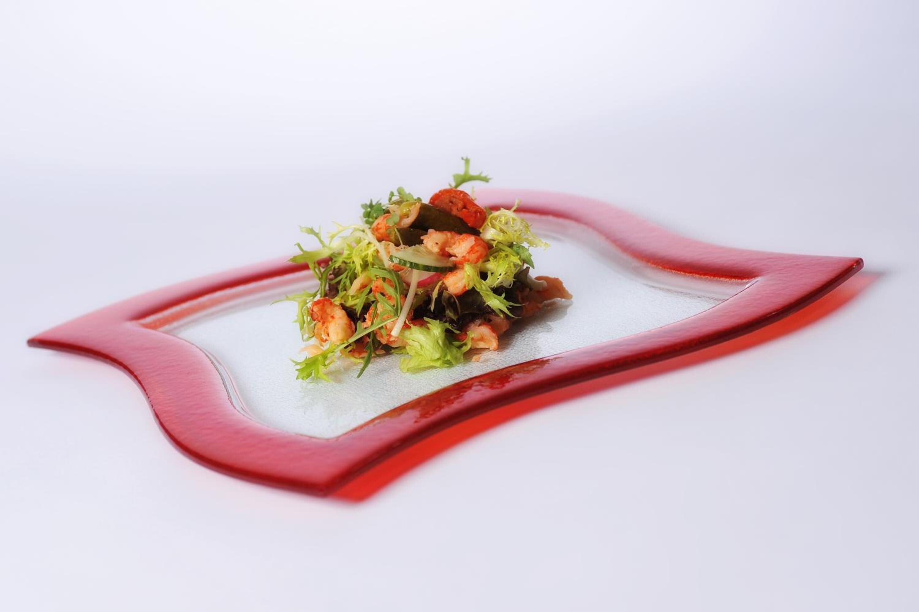 A dish with seafood and greens on a white plate with a red rim.
