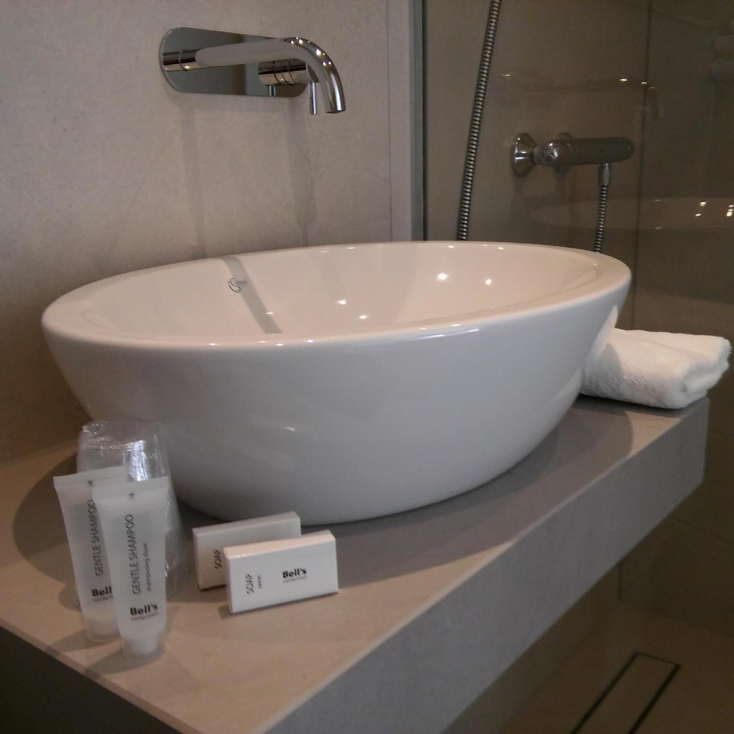 A bathroom with a large white vessel sink, a handheld showerhead, and a glass shower enclosure.