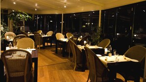 Ein Restaurant mit warmen Holzdielen und Korbstühlen. Die Tische sind mit Kerzen und Gläsern gedeckt.
