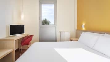 Habitación de hotel con cama, escritorio con computadora, una silla roja, ventana y radiador.