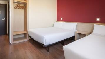 Habitación de hotel con dos camas, un armario de madera con perchas y una pared de acento roja.