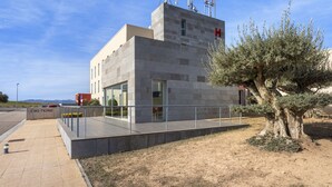 Un edificio moderno con fachada de vidrio, barandilla de metal y un árbol en primer plano.