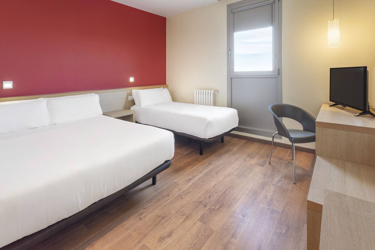A hotel room with two beds, a desk, a chair, and a television.