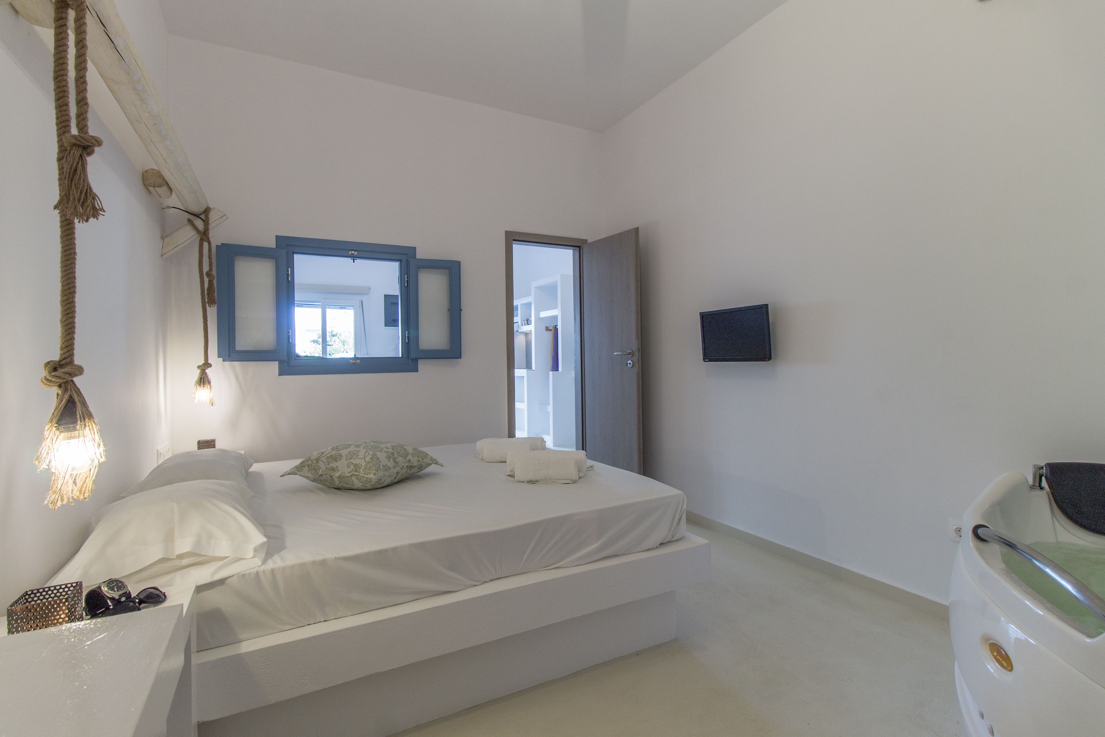 A bedroom with a bed, bedside table, lamp, and a TV mounted on the wall.