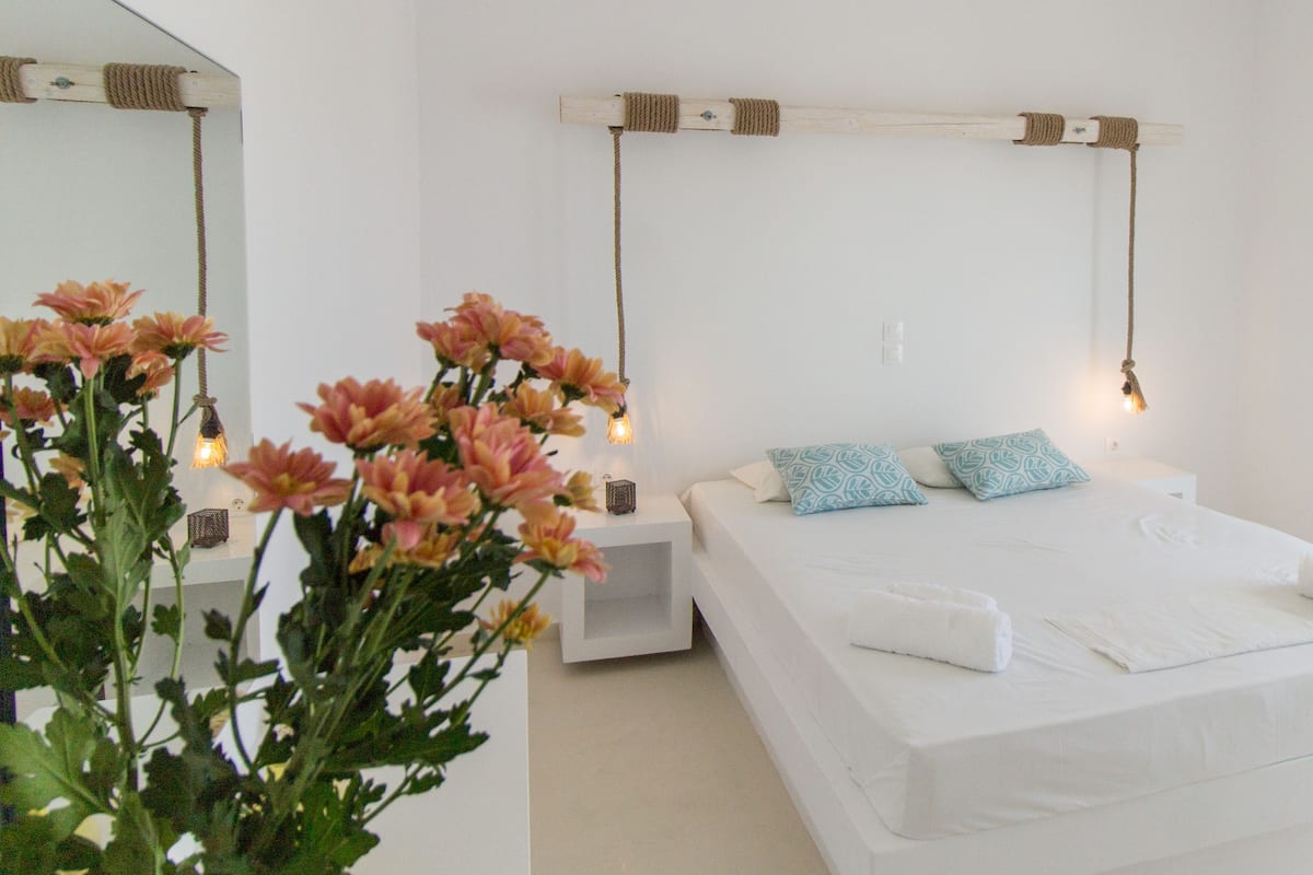 A bedroom with a large bed, two pillows, a bedside table, a nightstand, a hanging light fixture, and a mirror on the wall.