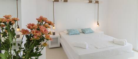 A bedroom with a large bed, two pillows, a bedside table, a nightstand, a hanging light fixture, and a mirror on the wall.