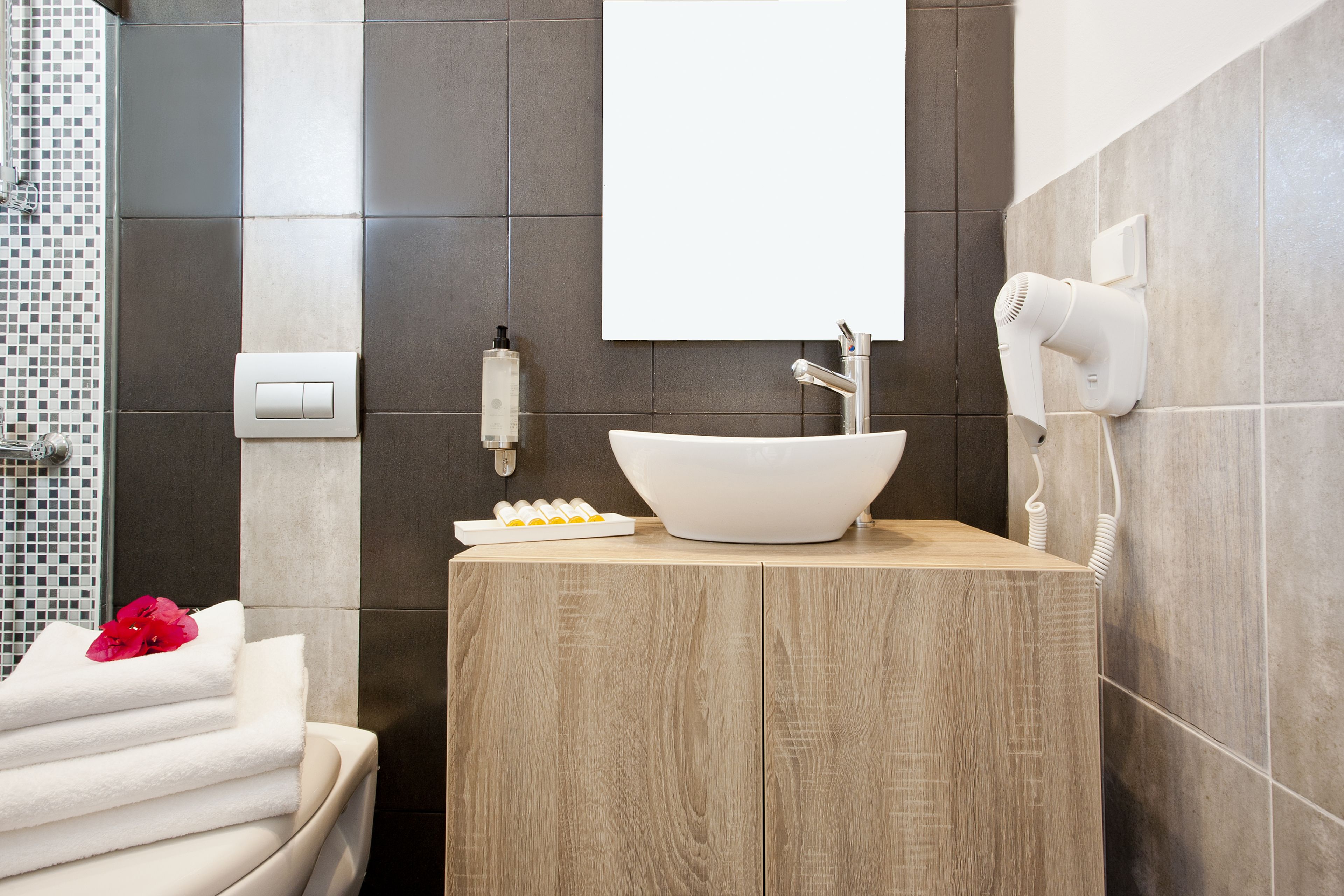 A modern bathroom with a wooden vanity, a white sink, and a hairdryer mounted on the wall.