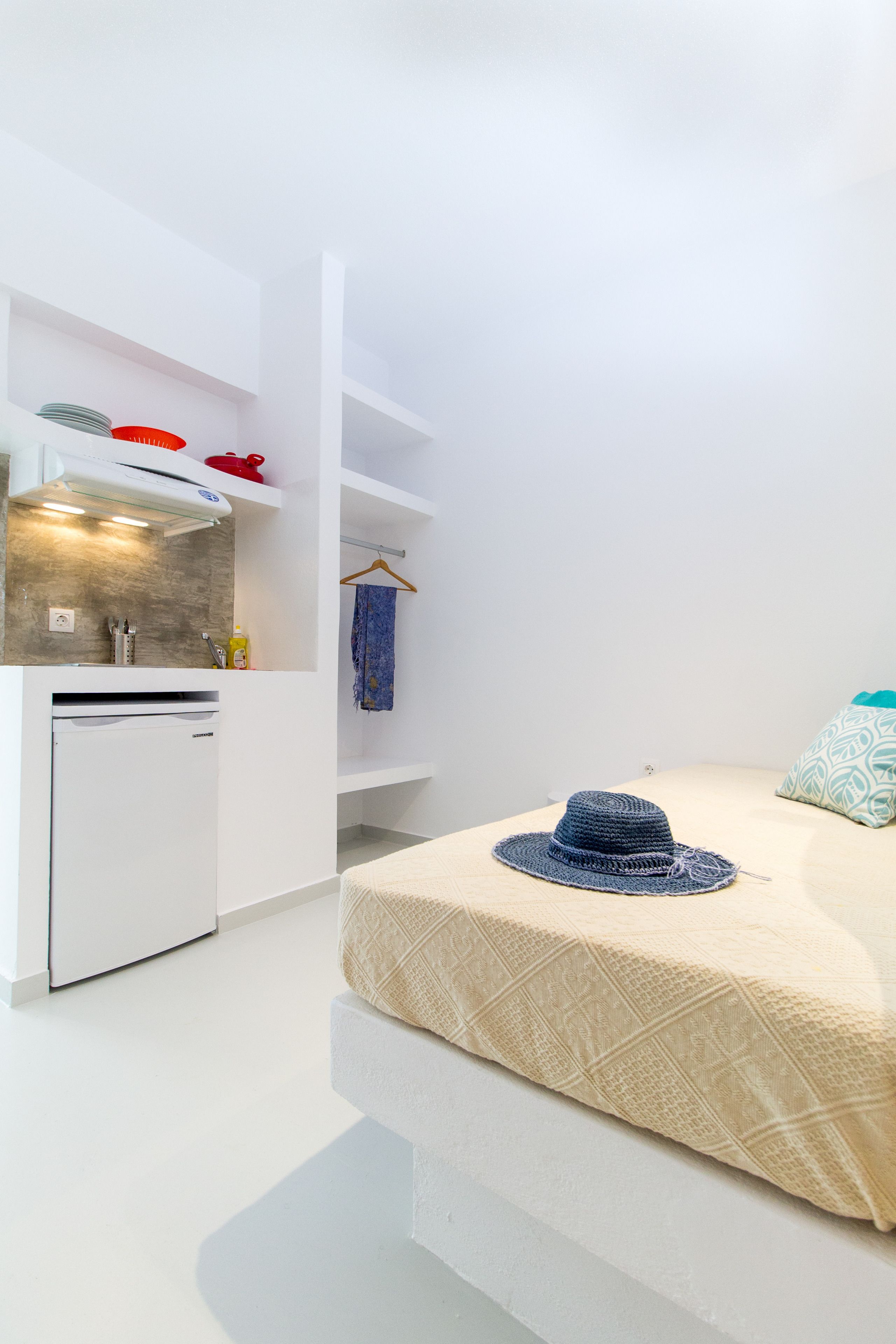 A compact room with a kitchenette, a bed with a patterned bedspread, and a hanging towel.